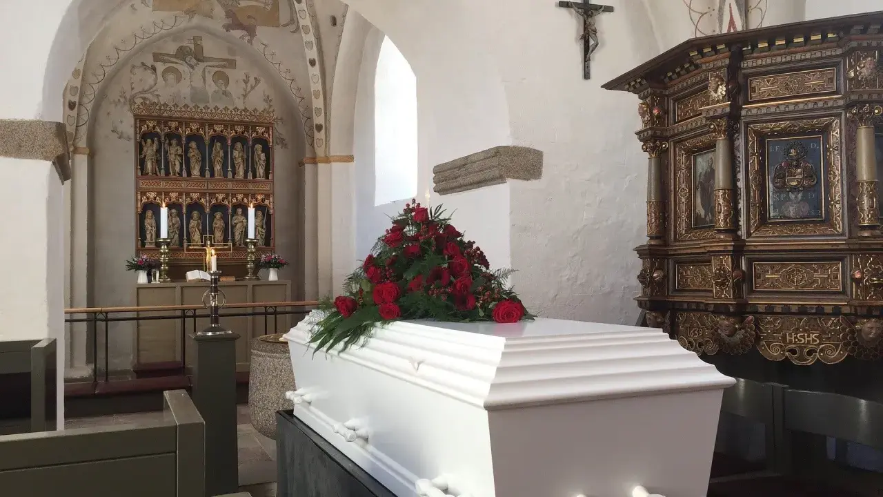 Biała trumna z czerwonymi różami w kościele. Warto wiedzieć, jak się zachować przy otwartej trumnie, by okazać szacunek zmarłemu.