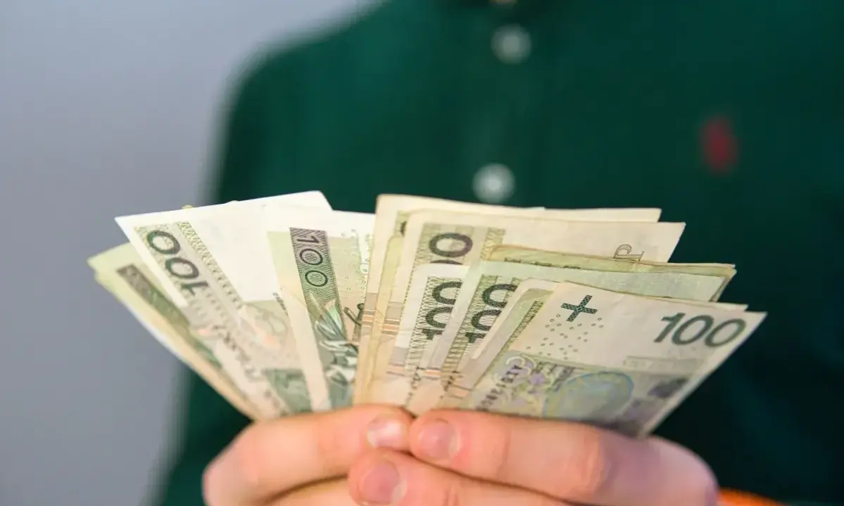 Dłonie trzymają plik banknotów 100 zł. Pytanie brzmi: ile wynosi renta rodzinna?