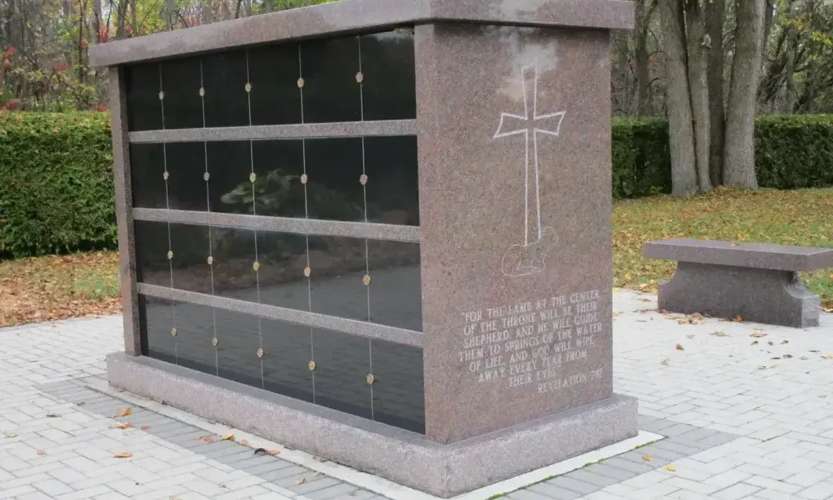 Kamienny grobowiec na urny z wygrawerowanym krzyżem i cytatem z Biblii. Obok ławka.