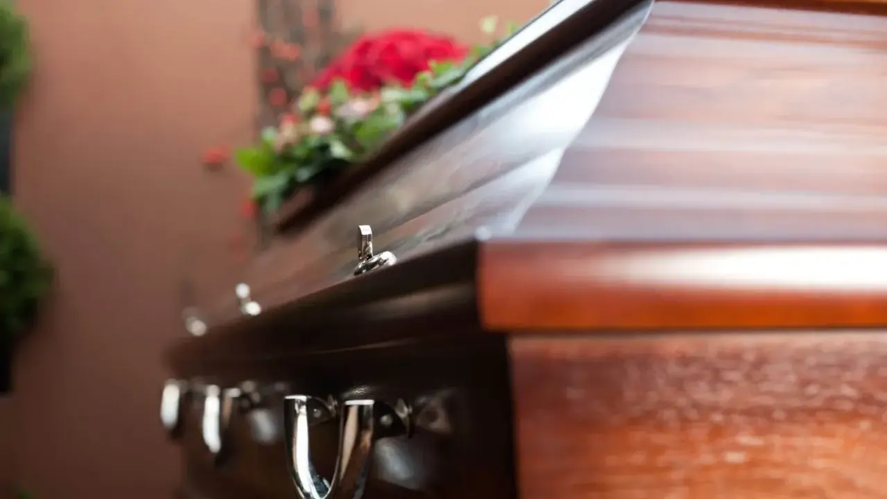 Drewniana trumna z kwiatami. Kto ma obowiązek pochować zmarłego? Prawo określa krąg osób odpowiedzialnych za organizację pogrzebu.