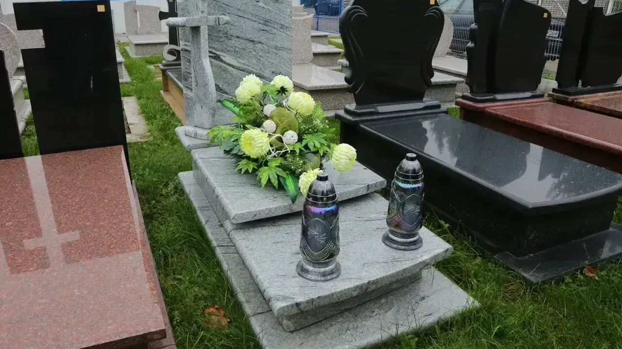 Elegancka dekoracja grobu bez pomnika: szare płyty kamienne, bukiet jasnych kwiatów i dwie ozdobne znicze.