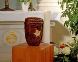 Elegancka urna z liściem klonu na drewnianym postumencie. Pytanie: czy można samemu przewozić urnę z prochami z zagranicy?