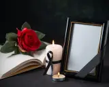 Pusta ramka na zdjęcie, płonące świece i czerwona róża na otwartej księdze. Symboliczne przedmioty wyrażające kondolencje.