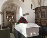 Biała trumna z czerwonymi różami w kościele. Warto wiedzieć, jak się zachować przy otwartej trumnie, by okazać szacunek zmarłemu.