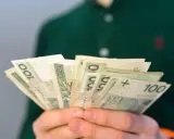 Dłonie trzymają plik banknotów 100 zł. Pytanie brzmi: ile wynosi renta rodzinna?