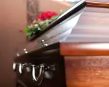 Drewniana trumna z kwiatami. Kto ma obowiązek pochować zmarłego? Prawo określa krąg osób odpowiedzialnych za organizację pogrzebu.