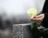 Dłoń trzyma białą różę przy nagrobku. Pytanie, jak długo nie można ruszać rzeczy zmarłego, wciąż pozostaje.