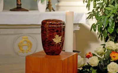 Elegancka urna z liściem klonu na drewnianym postumencie. Pytanie: czy można samemu przewozić urnę z prochami z zagranicy?
