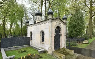 Elegancki, murowany grób z kopułami i ozdobnymi drzwiami, otoczony zielenią cmentarza.