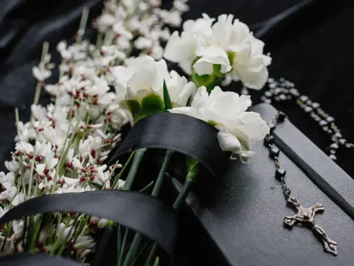 Białe kwiaty na pogrzeb, czarna wstęga i różaniec na czarnej tkaninie. Symbol żałoby i pamięci.