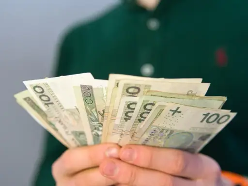 Dłonie trzymają plik banknotów 100 zł. Pytanie brzmi: ile wynosi renta rodzinna?