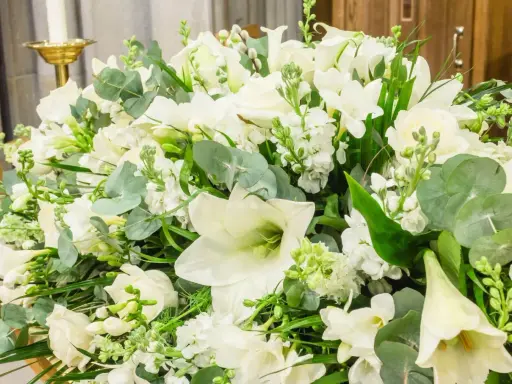 Piękna, biała wiązanka kwiatów z liliami, różami i zielonymi liśćmi.