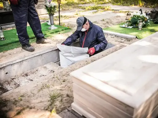 Ekshumacja zwłok po 40 latach. Pracownicy w masce i rękawiczkach wyciągają worek z grobu. Obok leży nowa trumna.