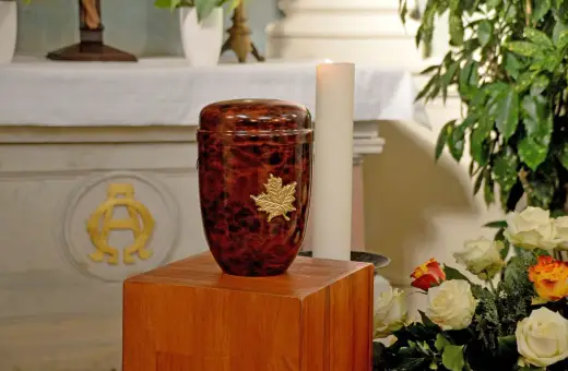 Elegancka urna z liściem klonu na drewnianym postumencie. Pytanie: czy można samemu przewozić urnę z prochami z zagranicy?