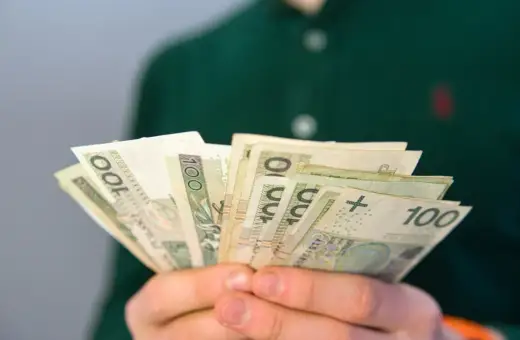 Dłonie trzymają plik banknotów 100 zł. Pytanie brzmi: ile wynosi renta rodzinna?