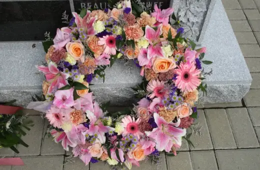 Piękna kompozycja funeralna z różowych lilii, róż i gerber, ozdobiona fioletowymi akcentami, spoczywa na kamiennej płycie nagrobnej.