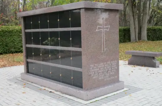 Kamienny grobowiec na urny z wygrawerowanym krzyżem i cytatem z Biblii. Obok ławka.