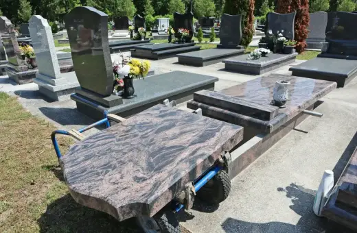 Na cmentarzu wózek transportuje płytę nagrobną. Kiedy można postawić pomnik po pogrzebie? Zwykle po kilku miesiącach, gdy ziemia osiądzie.