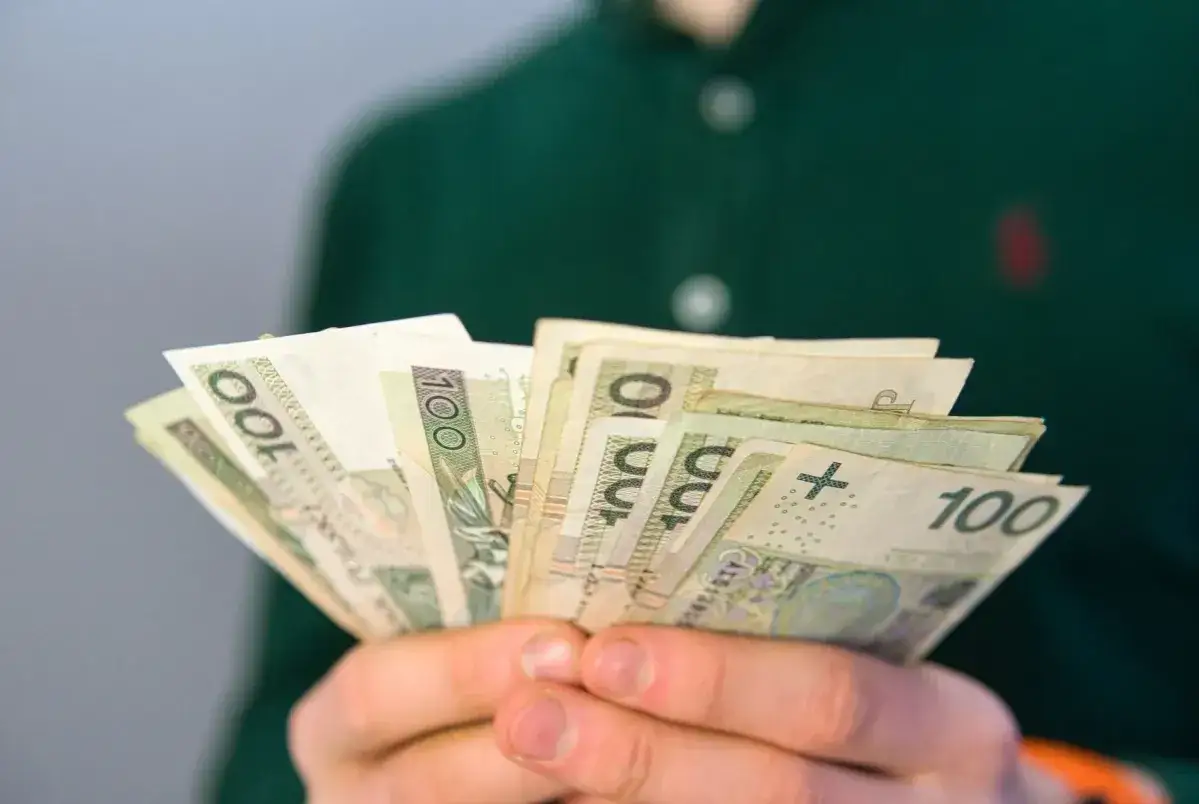 Dłonie trzymają plik banknotów 100 zł. Pytanie brzmi: ile wynosi renta rodzinna?