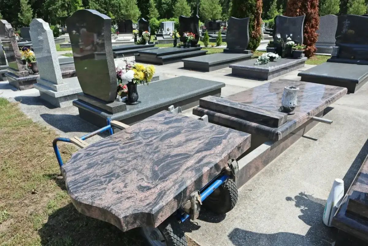 Na cmentarzu wózek transportuje płytę nagrobną. Kiedy można postawić pomnik po pogrzebie? Zwykle po kilku miesiącach, gdy ziemia osiądzie.
