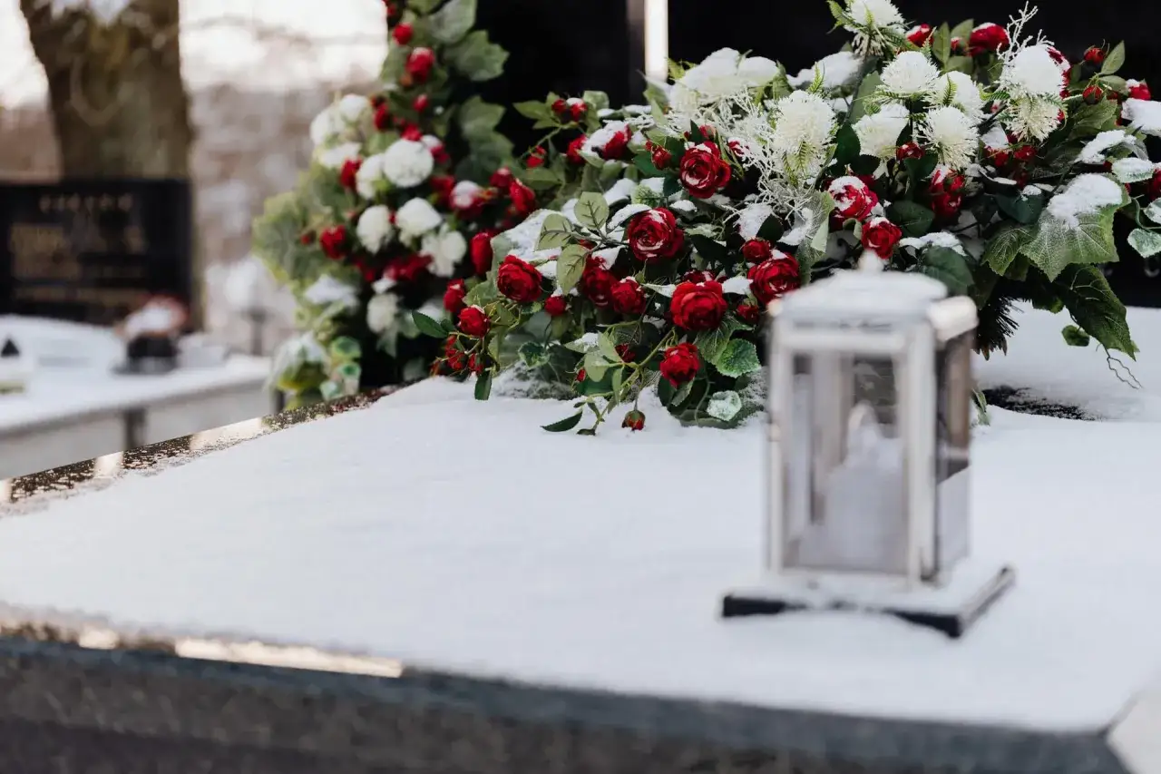 Zimowy cmentarz, śnieg na nagrobku, bukiet czerwonych róż i białych kwiatów. Cisza i zaduma, gdy zastanawiamy się, co się mówi na pogrzebie.