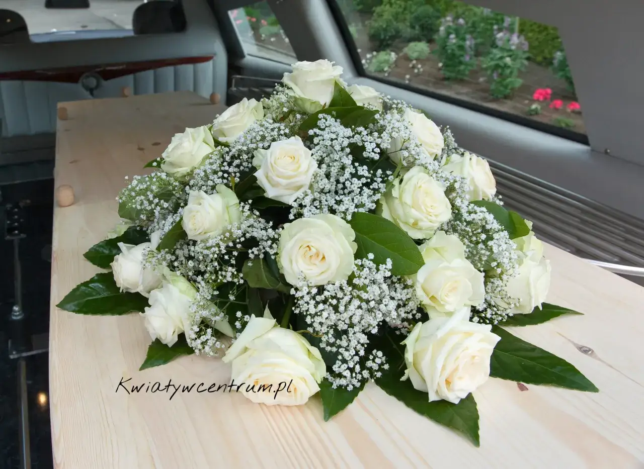 Elegancka kompozycja funeralna z białych róż i gipsówki na drewnianej trumnie.